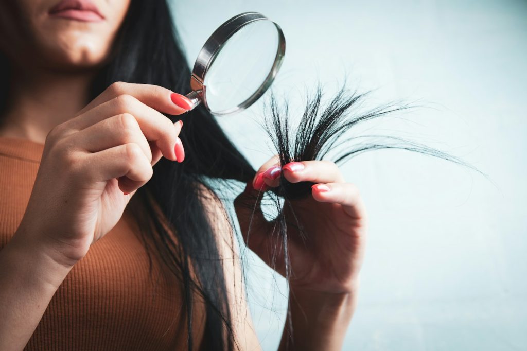 Woman examining the ends of her hair with a magnifying glass